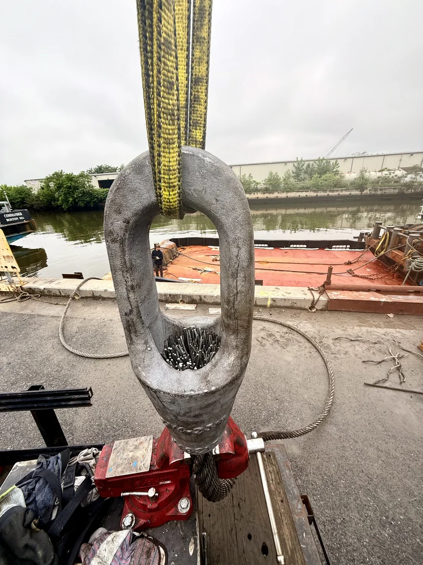A closed spelter socket on a pendant slung from a web sling at the dock, water and a barge behind